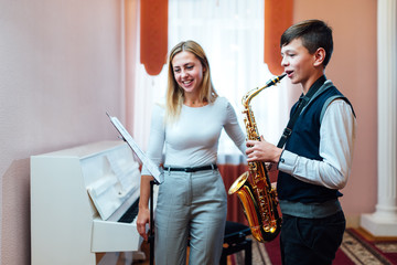 Cheerful teacher with student boy learning saxophone lessons at school