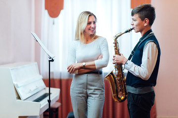 Cheerful teacher with student boy learning saxophone lessons at school