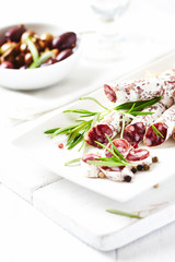 Sliced french salami with fresh rosemary and olives on white background.