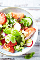 Healthy Salad with Cherry Tomatoes, Green Olives, Radish, Leek, Lettuce and Fresh Basil. Easy summer snack. Bright wooden background. Top view. 