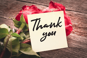 Close-up note with the words "Thank you" on a bouquet of red roses on a wooden background: the concept of gratitude and appreciation