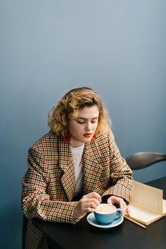 Woman with book stirring coffee in cafe
