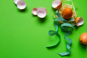 Brown chicken egg in a straw nest, broken eggshell and green checkered ribbon, minimalistic easter background or concept