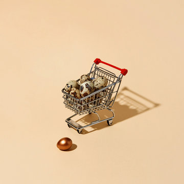 Colored golden egg and shopping cart with quail eggs on a beige background with copy space. Profit concept