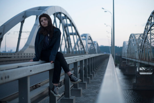 girl sitting on the railing on the background of the bridge