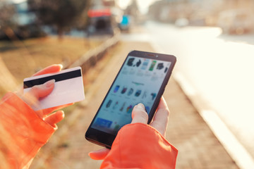 The concept of online shopping. Women's hands hold a smartphone with a blurred screen, and a Bank card, making purchases online in the online store