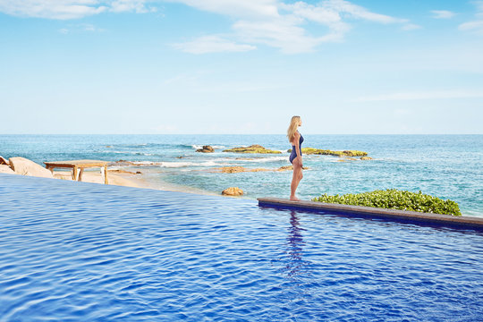 Woman standing on edge of infinity swimming pool at the beach