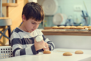 Cute boy decorating holiday gingerbread cookies at home kitchen