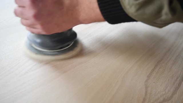 Man sanding wood with orbital sander in a workshop
