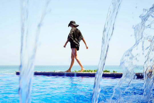Woman standing on edge of infinity swimming pool at the beach