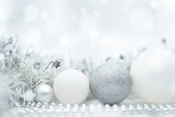 A festive design of silvery and white Christmas ornaments under a winter effect bokeh and snow background with copy space