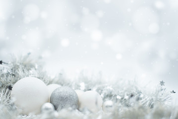 A festive design of silvery and white Christmas ornaments under a winter effect bokeh and snow background with copy space