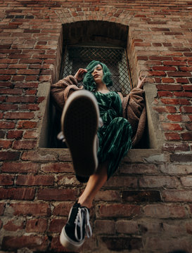 Beautiful woman with green hair sitting on a ledge of a brick wall building outside in the city