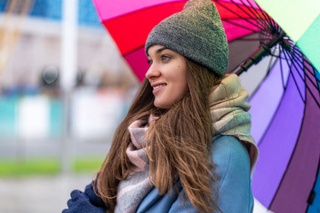Portrait of happy smiling joyful carefree woman in warm clothes with bright multicolored rainbow umbrella during rainy day and rain weather in the autumn. Rain protection