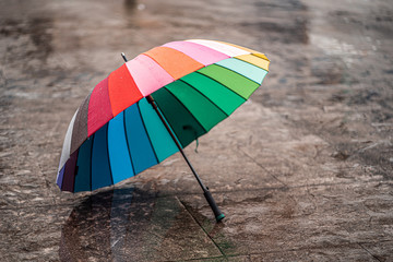 Rainbow umbrella on wet asphalt during cold weather in autumn rainy day in the fall. Rain protection