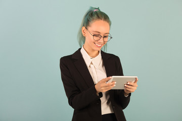 beautiful young woman in glasses and a black suit on a blue background with a tablet in hand