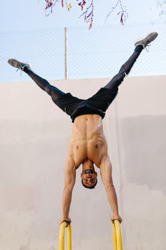 Young sportive man doing handstand near grey wall