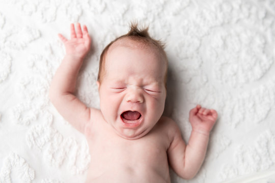 A baby with a big yawn laying on a chenille blanket