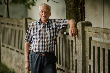 Elderly man in plaid shirt leaning on fence