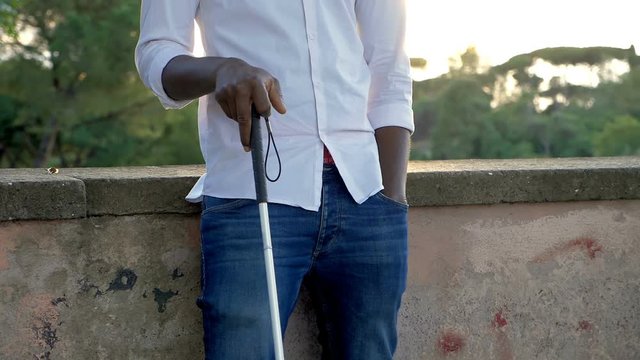 blind black young man with his white stick at sunset