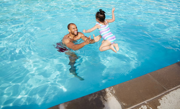 Young girl jumping into her father's arms in a swimming pool
