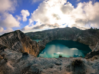 Fototapeta na wymiar View on the Kelimutu volcanic crater lakes in Flores, Indonesia. Lakes are shining with many shades of turquoise and blue. Sun shines through clouds. Barren and sharp slopes of the volcanic crater