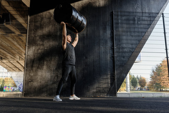 Brutal sportsman training with barrel on sports ground