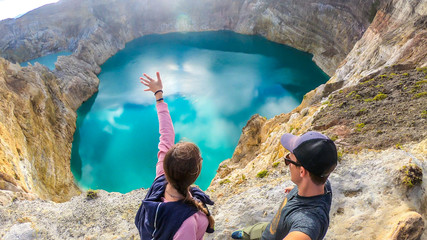 Couple standing at the volcano rim and watching the Kelimutu volcanic crater lakes in Moni, Flores, Indonesia. They are having fun, enjoying the view on lake shining with many shades of turquoise © Chris