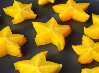 Fototapeta premium Fresh ripe starfruit or Averrhoa carambola cut in stars on a dark plate close up. Healthy food, vegetarian or diet concept.Exotic fruit background.