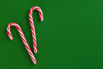 Two christmas red and white candy canes on green paper background.