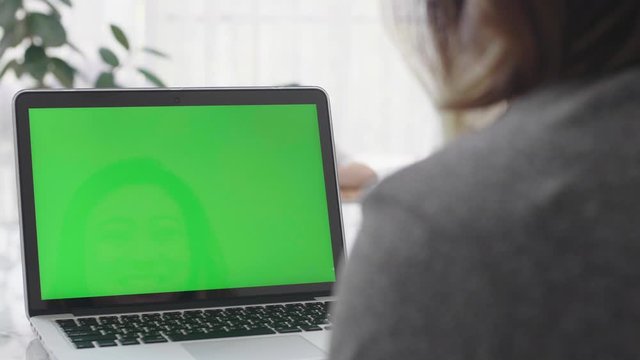 Over the shoulder shot of Asian woman looking at green screen. Office person using laptop computer with laptop green screen, 4K dolly shot
