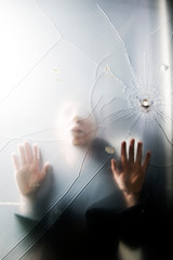 Person trapped behind cracked glass with bullet hole