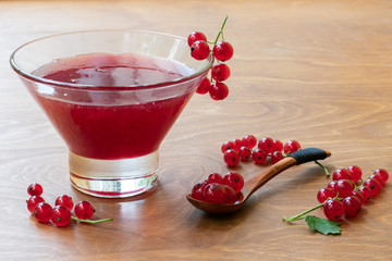 Glass bowl of red current jam with wooden spoon full of many ripe juicy red current berries on dark wooden table background. Marmalade made of fresh red current