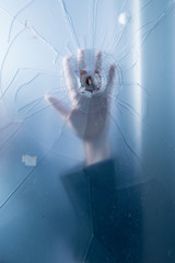 Conceptual photo of silhouette of hand behind glass with bullet hole