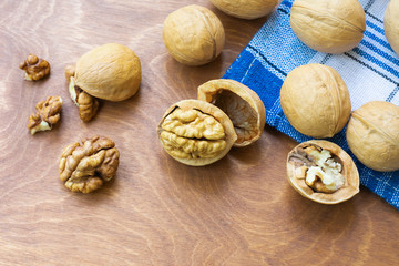 Whole walnuts and walnut kernel halves without shell on a dark wooden table and checkered towel,...