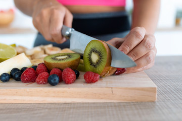 Woman's hands cutting kiwi on a wooden table.
