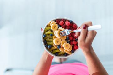 Woman's hands holding a bowl with fresh fruit while standing at home.