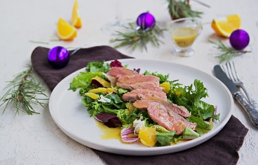 Warm salad with a mixture of salad leaves, baked duck and orange on a clay plate on a light concrete background in the New Year or Christmas style. Salad recipes with duck. Holiday recipes.