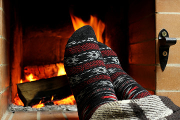 A woman warms her feet in knitted socks by the fireplace on a winter evening