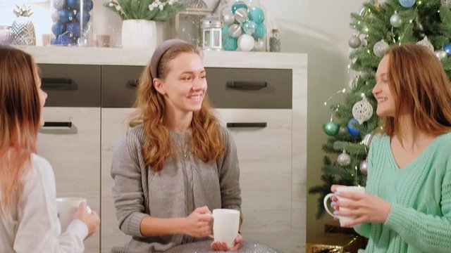 Festive gathering. New Year home party. Cheerful teen girls drinking tea enjoying conversation.