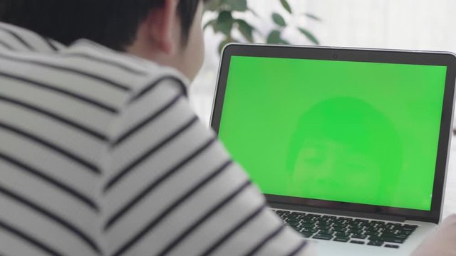 Over the shoulder shot of Asian boy looking at green screen. Home Office person using laptop computer with laptop green screen, 4K dolly shot