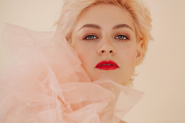 Headshot portrait of charming young woman with short blond hair and red lips looking at camera