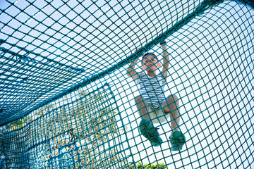 Little boy enjoy climbing the net in playground under sunshine