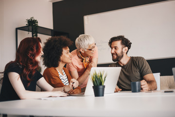 Multi-ethnic group of four entrepreneurs talking about business ideas gathered around desk with laptop on it.