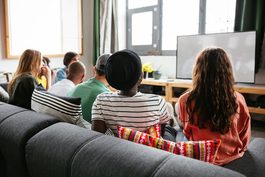 Friends sitting on sofa watching tv.