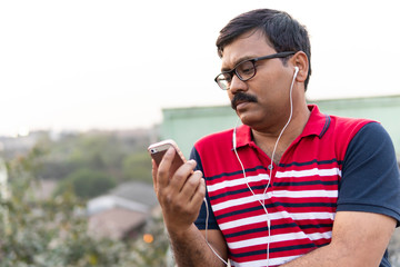Middle aged man listening music in a smartphone with a headphone
