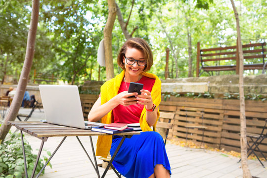 Happy Woman Using Laptop And Smartphone At Summer Outdoor Cafe.Happy Woman Working Using Multiple Devices On A Desk. Happy Confident Entrepreneur Working With A Laptop Gesturing 