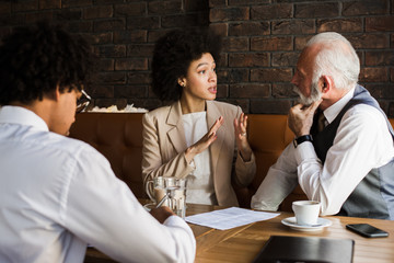 Two young business-people of African ethnicity talking with older executive in coffee shop.