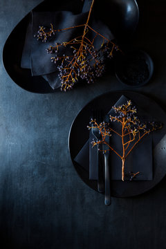 Dramatic table setting with black crockery, black paper stationery, twigs, berries and linens. Festive table decoration idea
