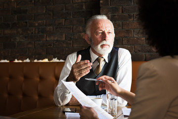 A senior expert telling a young businesswoman how to spread her business. in a cafe She is holding a pen and a piece of paper.